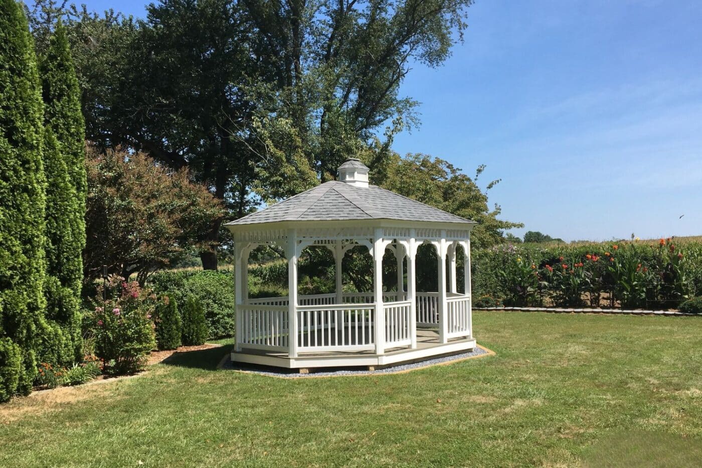 View of 12x16 Vinyl Oval Gazebo in garden during the day with gray roof and white vinyl
