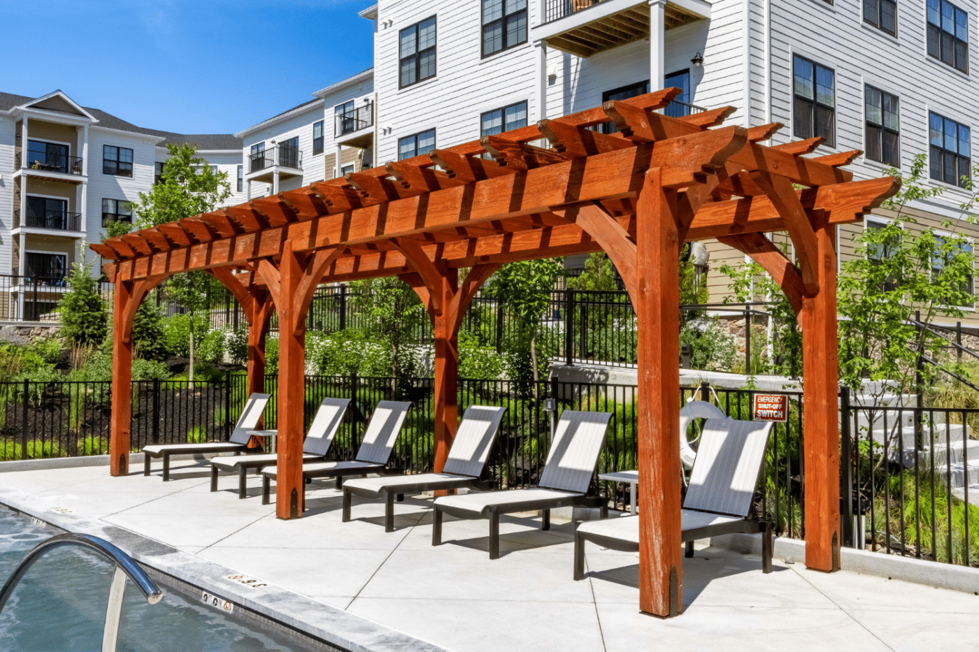 7x30 Boulder Pergola by pool next to apartment building, pool chairs placed underneath pergola