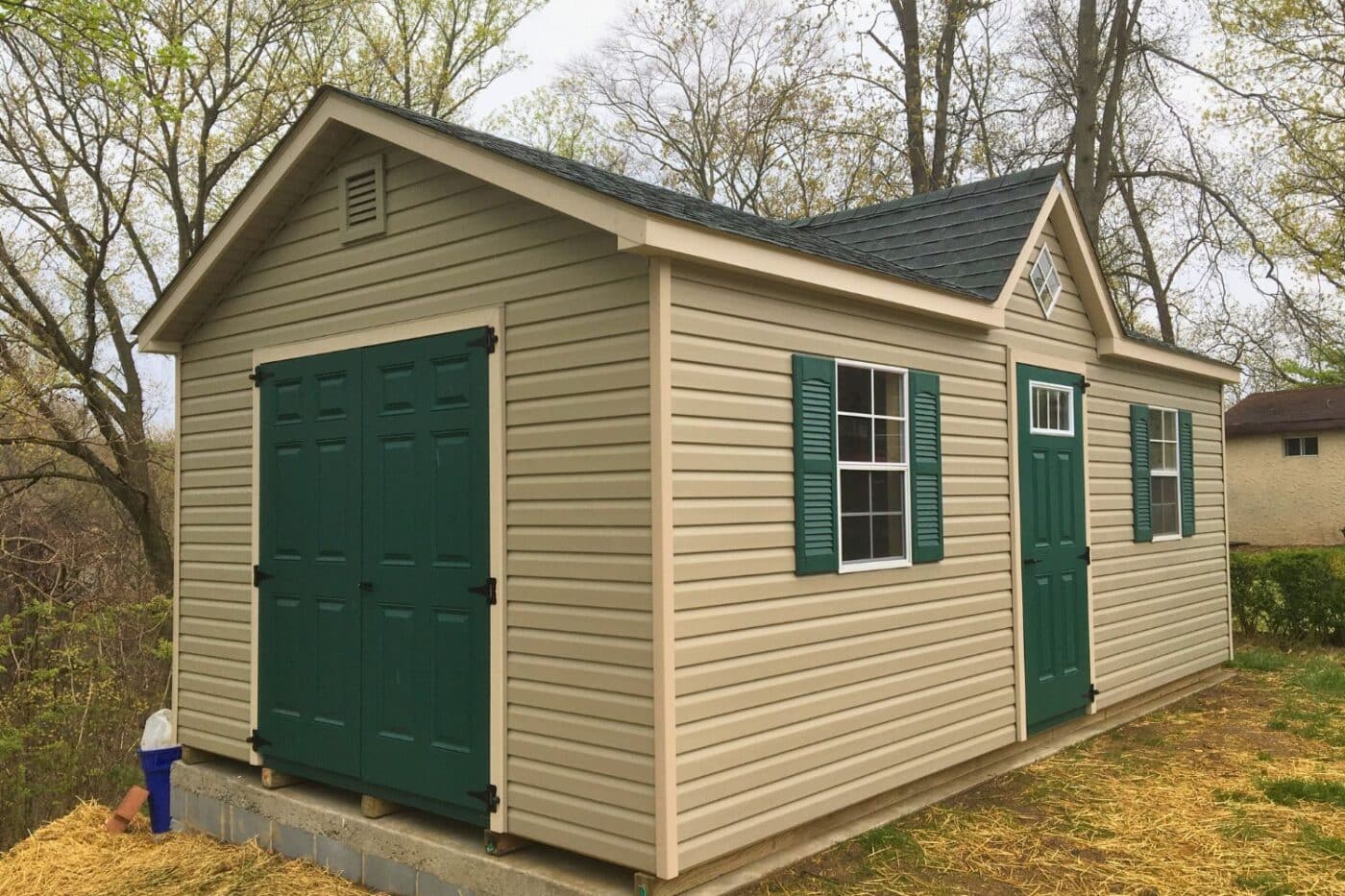 The Cape Cod Shed 3 Vinyl cape cod shed with green doors and shutters on concrete blocks in backyard