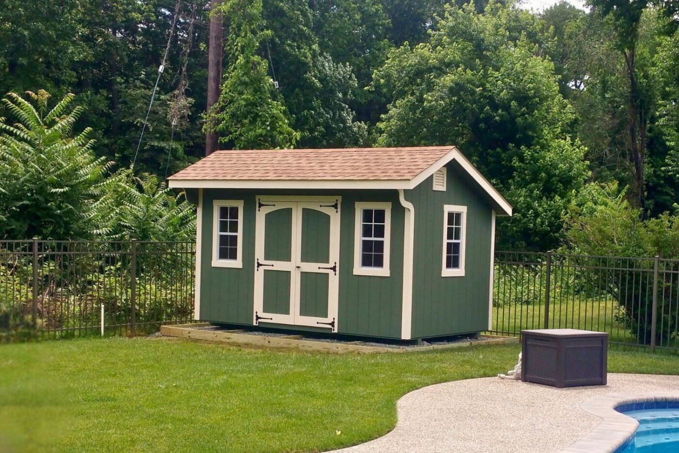 Designer carriage shed by pool with green siding and beige trim