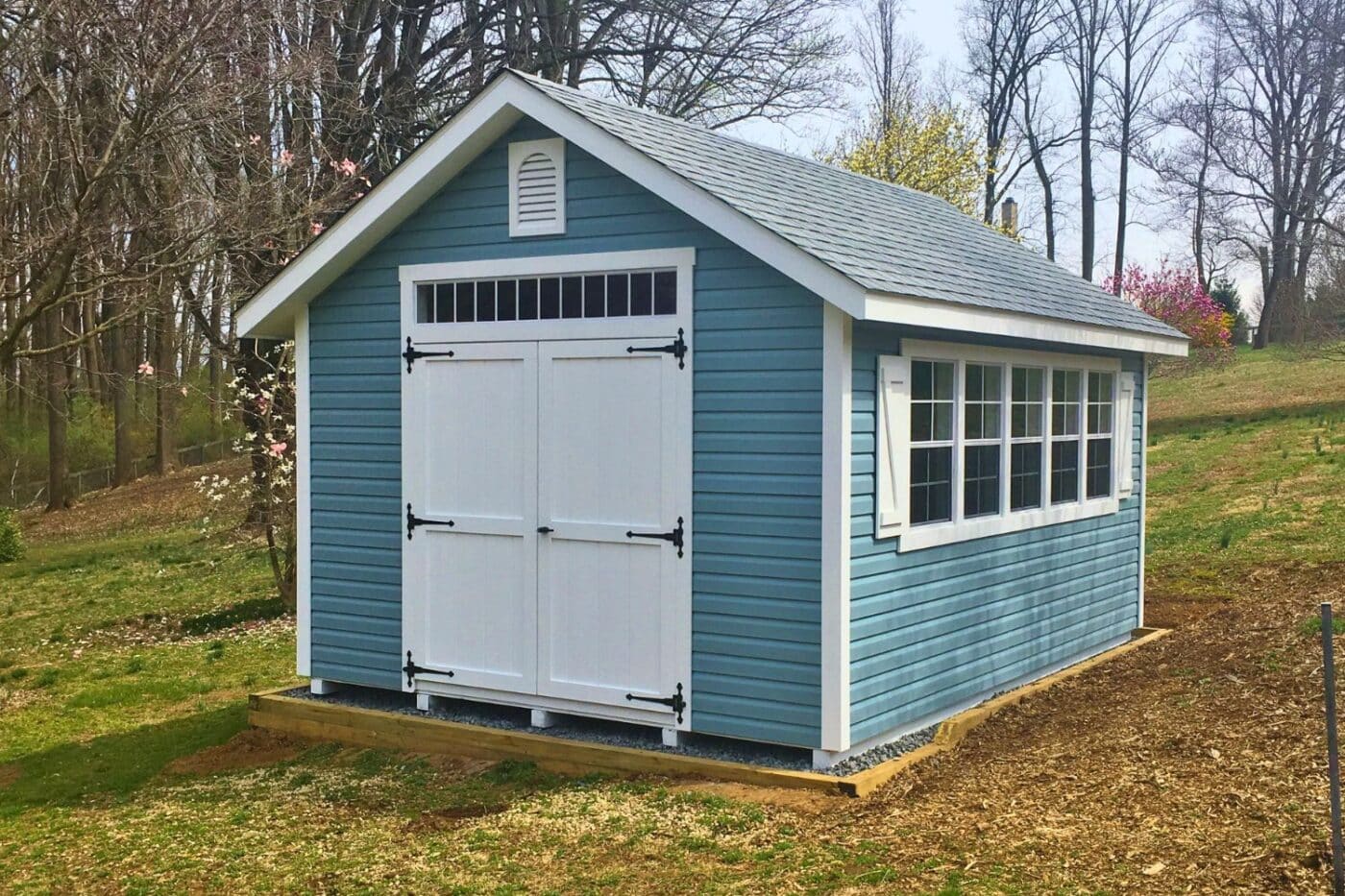 Blue and white designer shed with white double doors, asphalt shingles, and a transom window