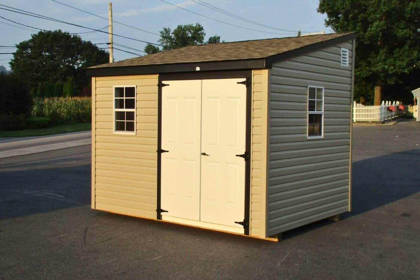 The Lean-To Shed 3 Vinyl Lean-to shed in parking lot bathed in sunlight with white double doors and black trim