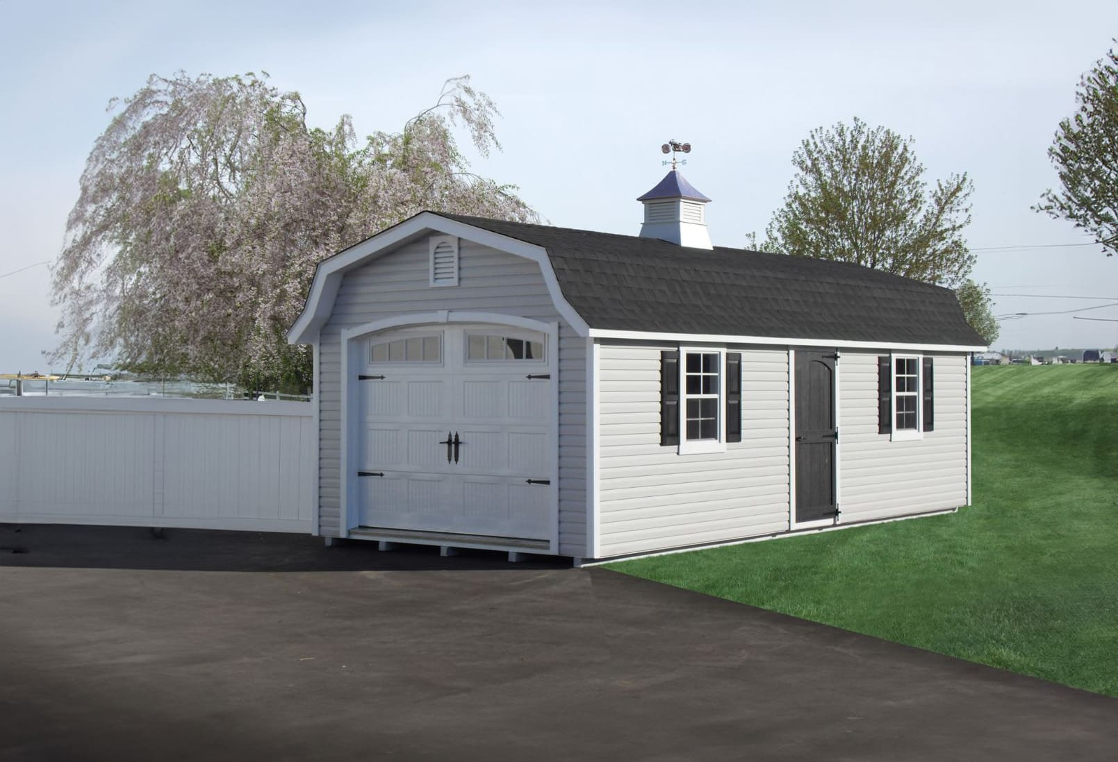 The Designer High Barn Garage 4 White vinyl designer high barn garage shed in grass and driveway with cherry blossom trees and white fence
