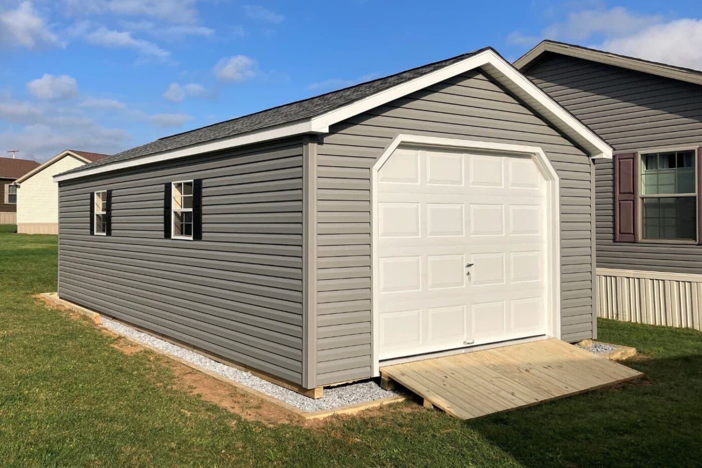 The Standard Workshop Garage 3 Vinyl garage shed with two windows, a white garage door, and ramp with black shutters