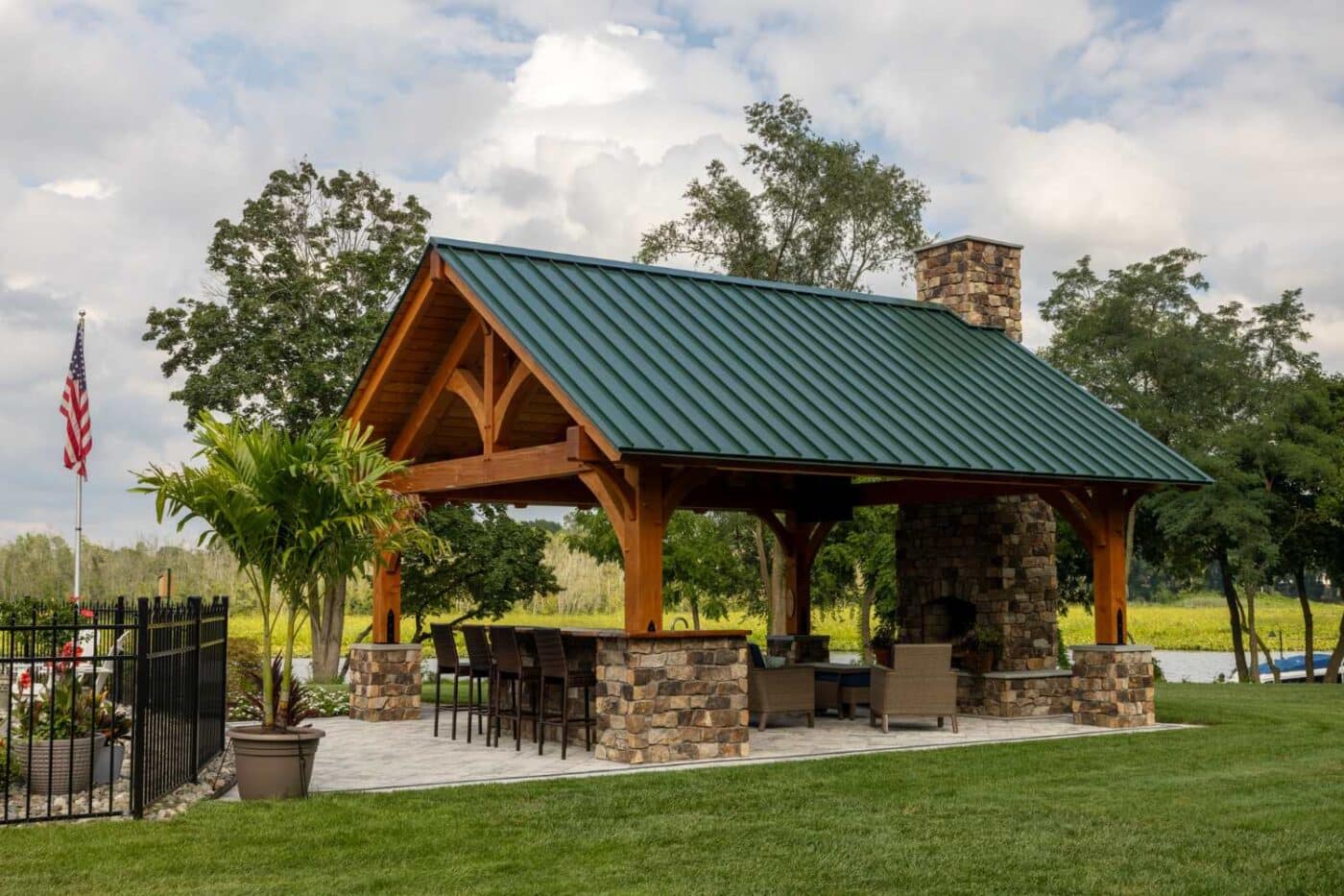 Sizes 1 Kingston Pro Timber Frame Pavilion on patio besides fence with flag
