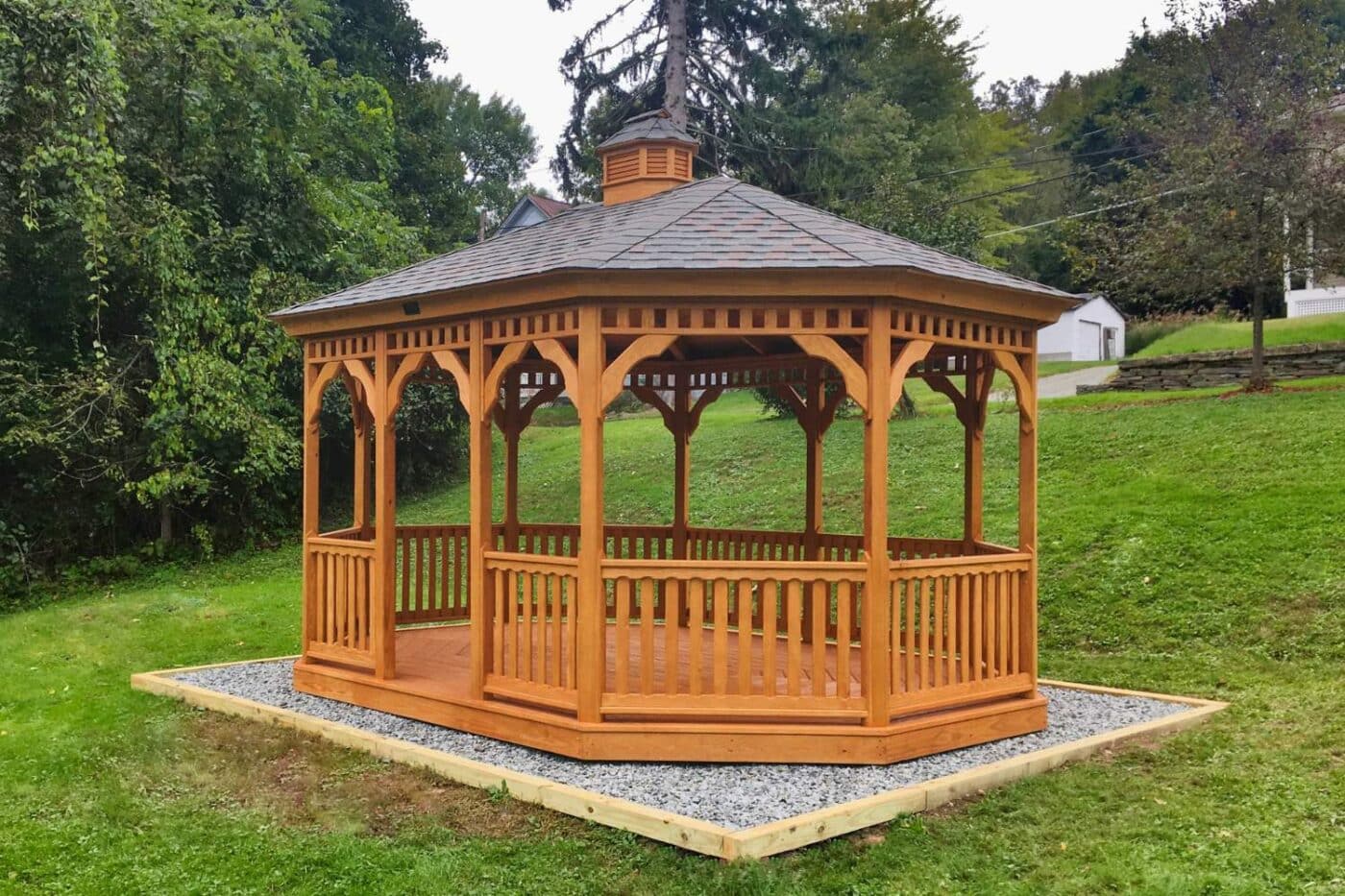 Wood Oval Gazebo on gravel pad besides trees