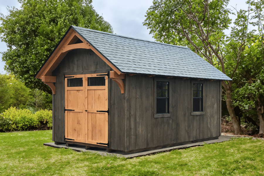 lancaster timber frame shed with gray siding and shingle roof featuring double wooden doors with transom windows